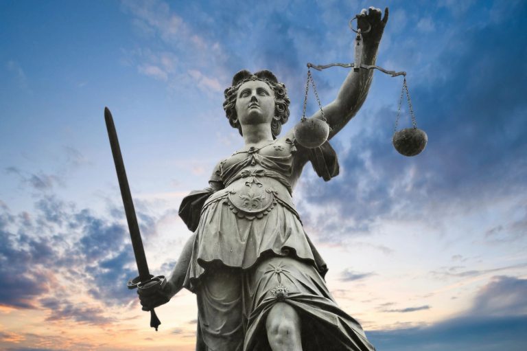 Statue of Lady Justice holding scales and a sword against a blue sky