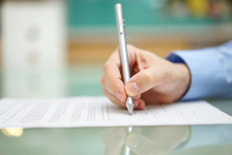 A hand signing a document with a pen